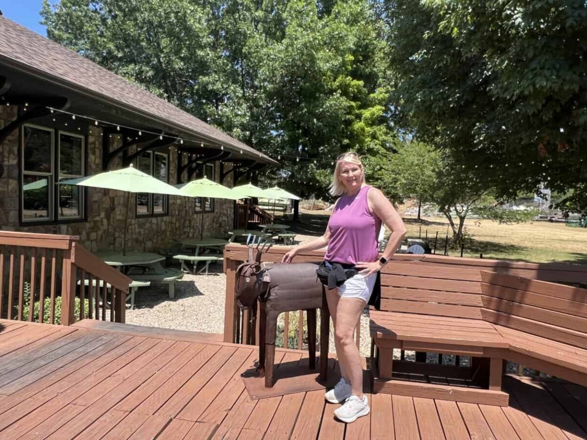 A woman poses for a picture with a goat sculpture on a wooden deck.