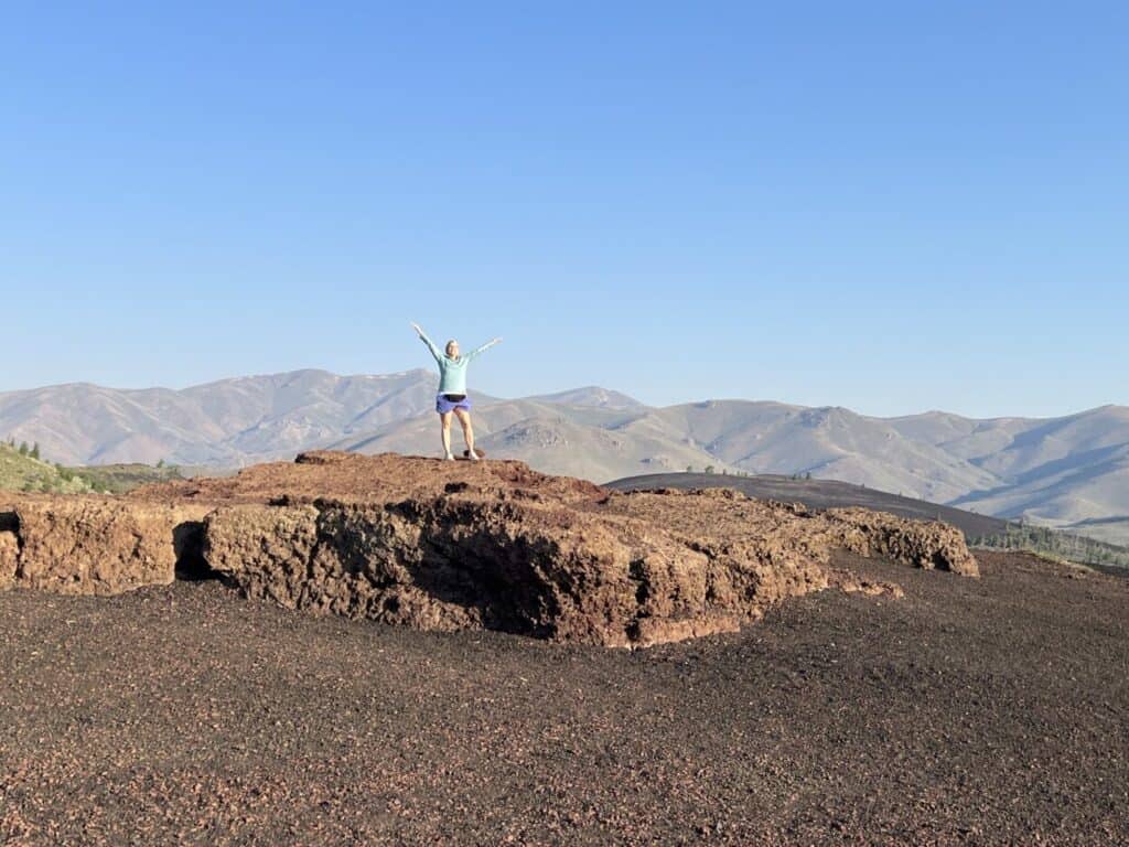 A woman raises her arms in triumph after climbing to the top of Inferno Cone.