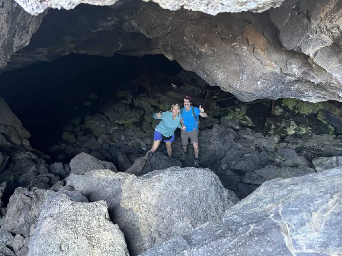 Julie McConkey and Scott McConkey of the Miles with McConkey Travel Blog each give a thumbs up from the inside of Dewdrop Cave, Craters of the Moon National Monument and Preserve, ID.