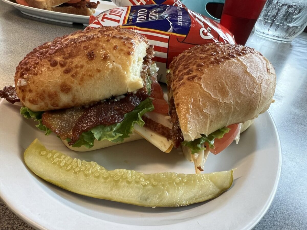 A sandwich, pickle, and bag of potato chips sit on a white plate