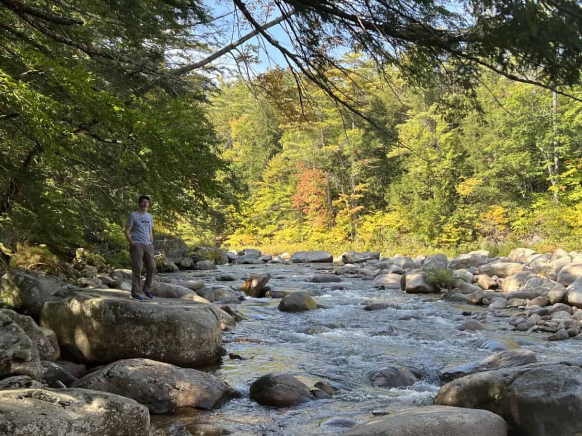 A man walks onto a large rock to get a close look at a river.