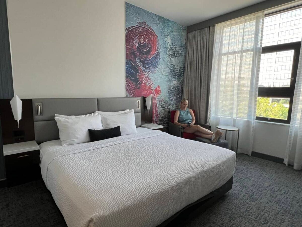 A woman sits on a chair in a hotel room with art on the wall behind her.