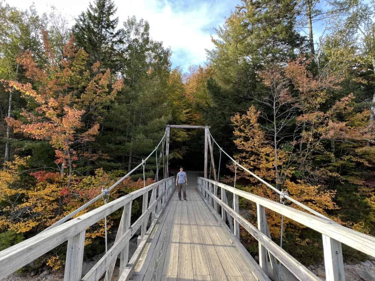 Scott McConkey, travel writer and founder of the Miles with McConkey Travel Blog, walks on a wooden suspension bridge in New Hampshire.