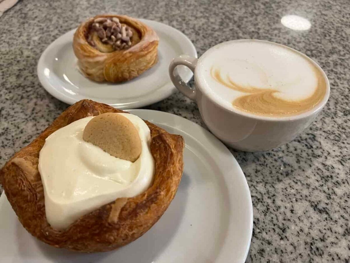 Two plates, each with a pastry, and a cup of coffee sit on a marble table.