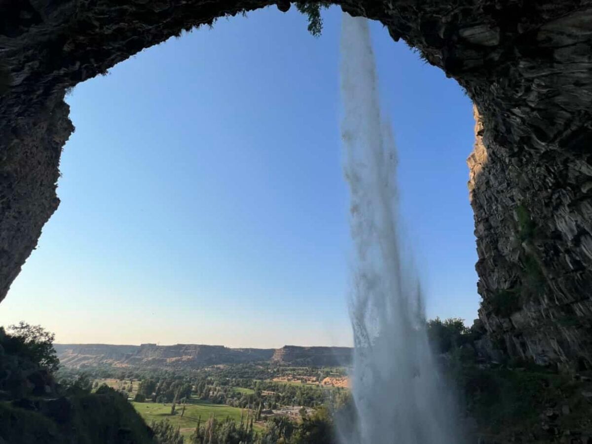 View from behind a waterfall overlooking a large grassy valley.