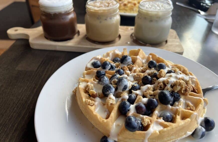 A coffee flight and a plate with a waffles topped with blueberries sit on a table.