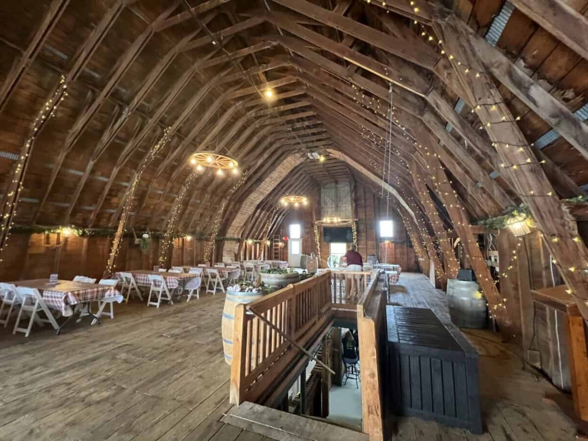 The upper floor of a barn contains tables and chairs under string lights.