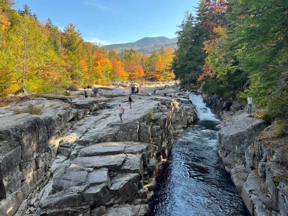 Visitors walk on top of rocky cliffs above a rushing river in the gorge below.