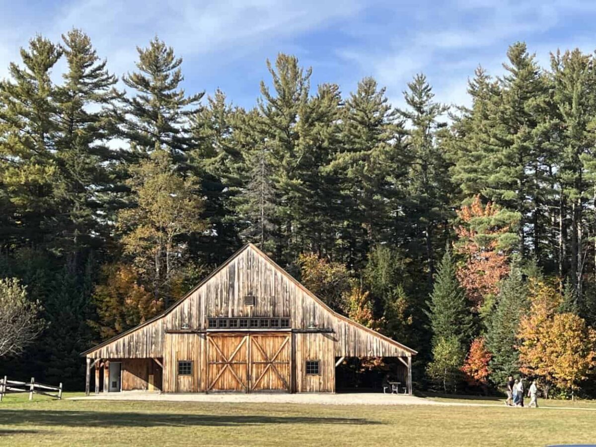 People walk on a paved path near a wooden farmhouse.