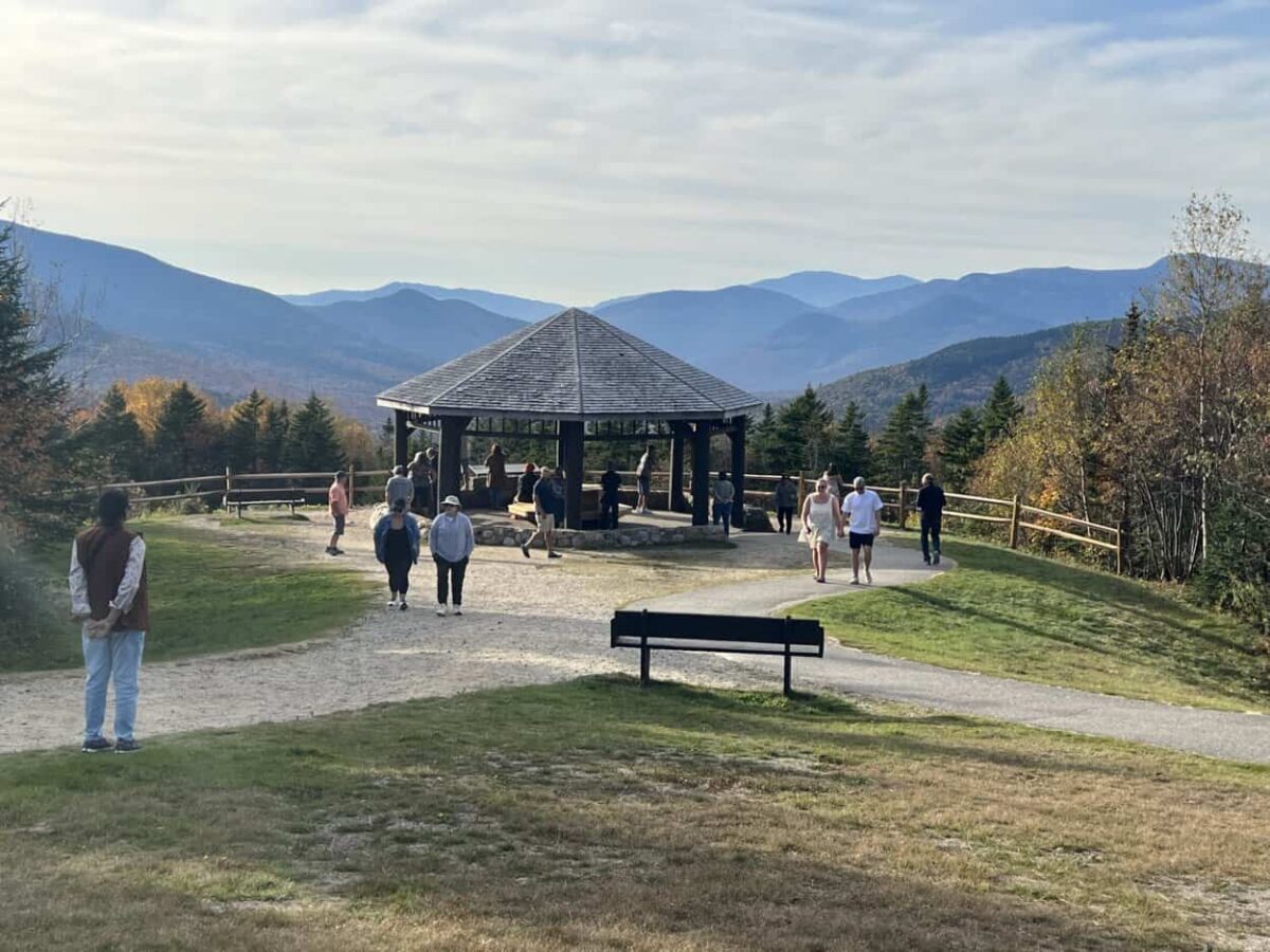 People stand under a shelter with a round roof to view mountains in the distance.
