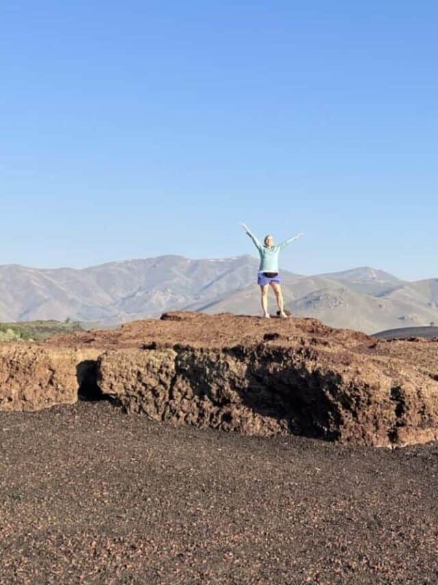 A woman raises her arms in triumph after climbing to the top of Inferno Cone.