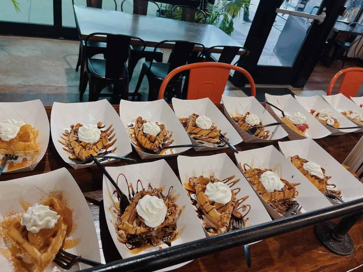 Food cartons with various waffles sit on a table.