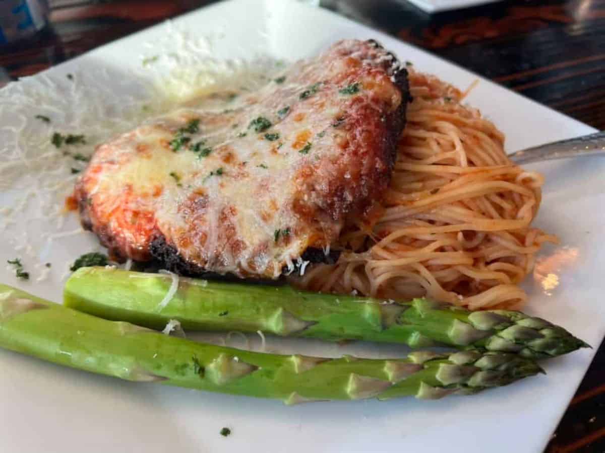 A white dinner plate contains chicken parmesan, spaghetti, and asparagus.