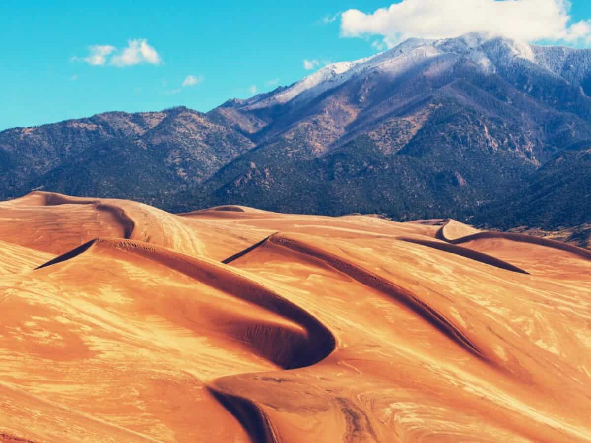 A mountain stands tall on the horizon with sand dunes in the foreground.