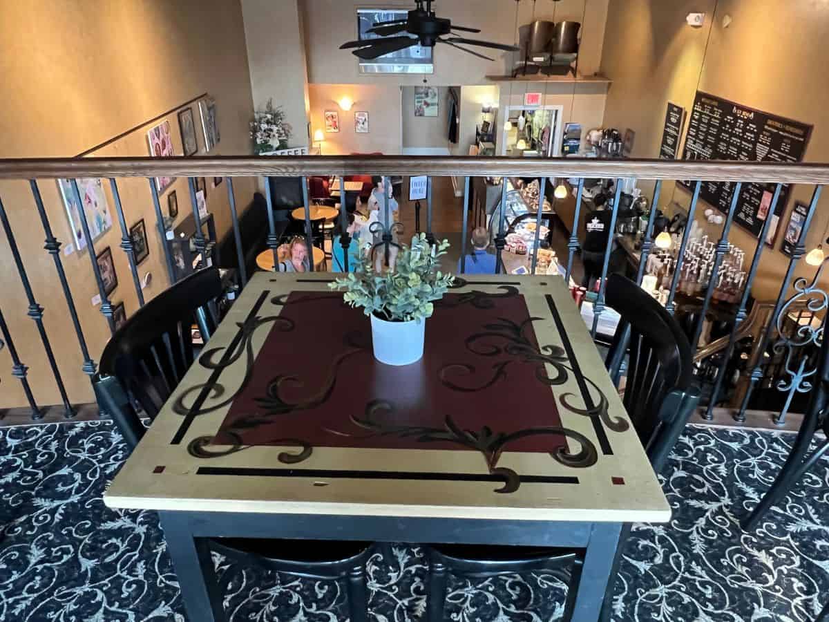 A plant sits on a table in the upper level of a coffee house while customers wait in line below to order.