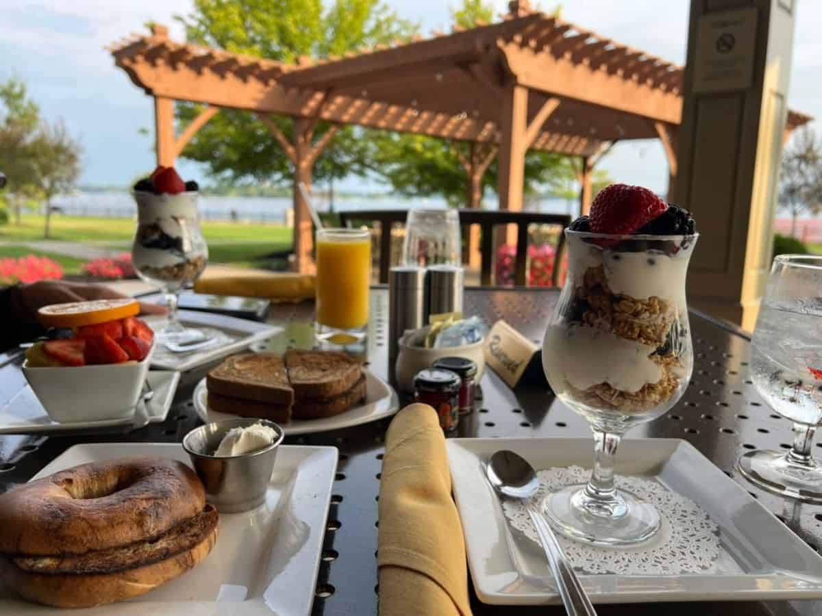A table contains breakfast items with a pergola and a river in the background.