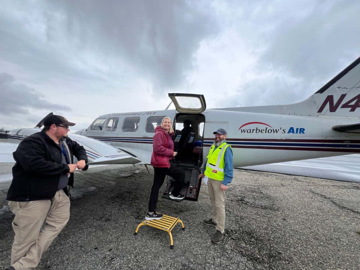 A woman turns to smile as she boards a small plane.