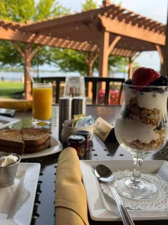 A table contains breakfast items with a pergola and a river in the background.