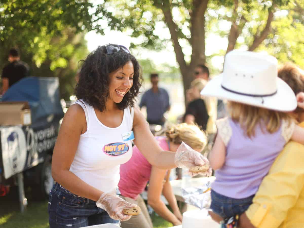 A woman hands a cooke to a little girl wearing a cowboy hat being held by a parent at the Mandan Rodeo Days festival.