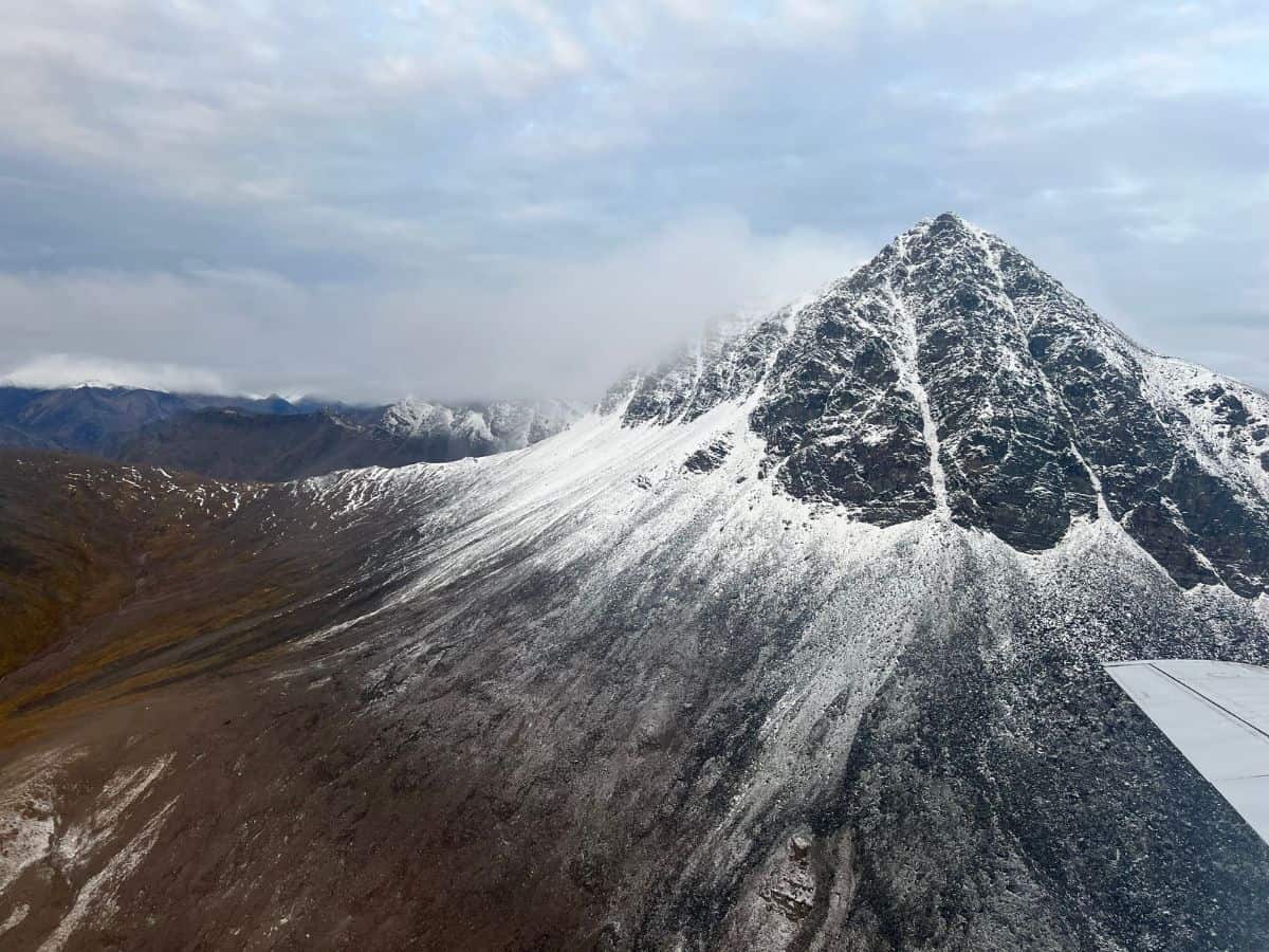 A plane flies close to a snowy mountain in Gates of the Arctic National Park Alaska.