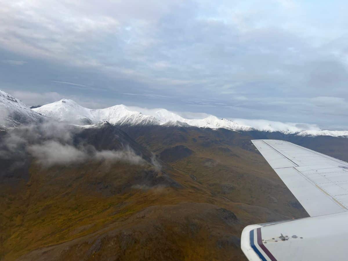 Snowy mountains line the horizon as a plane flies by in the foreground.