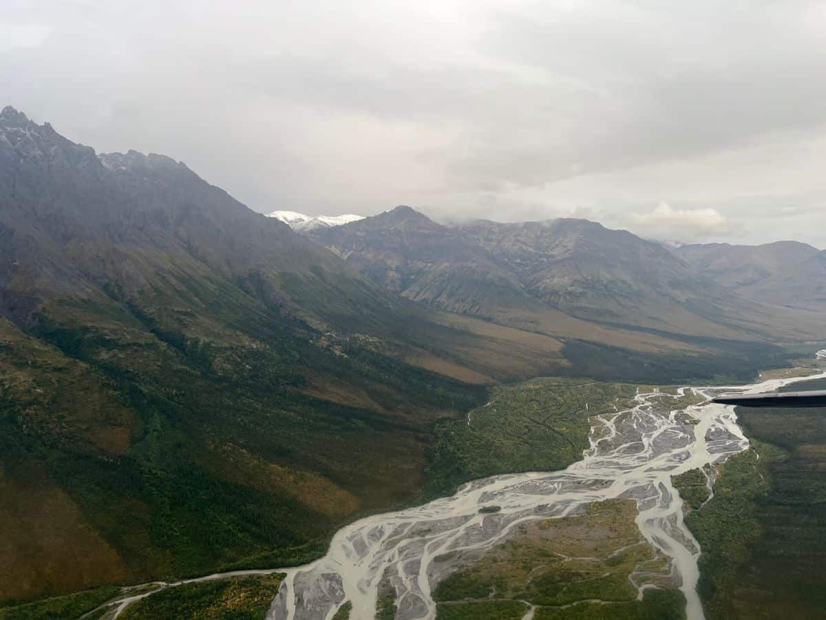 A large river running between mountains is partially frozen as seen from a plane.