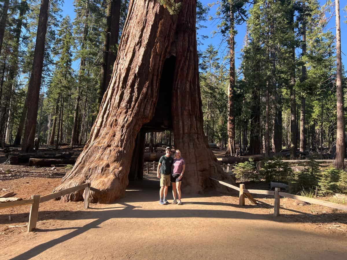 A man and woman pose for a picture in front of the California Tunnel Tree in Yosemite National Park