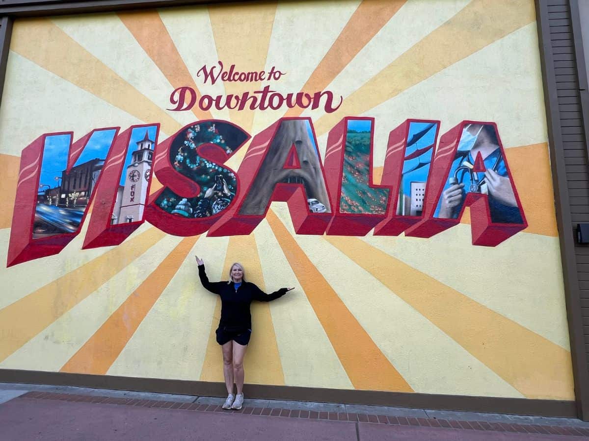 A woman poses with the "Welcome to Downtown Visalia" sign for pictures.
