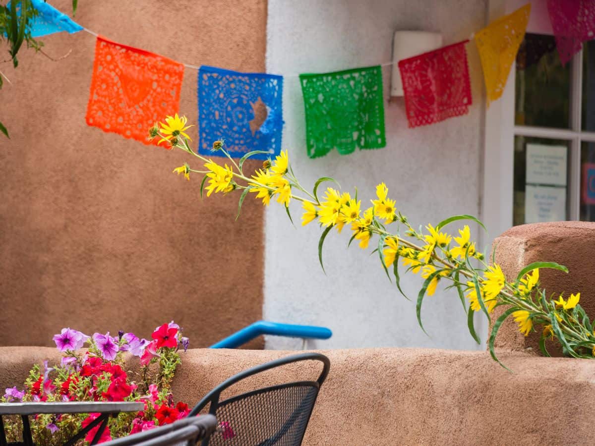 Colorful flowers sit on a table and a string of colorful napkins stretch across the ceiling against an adobe wall