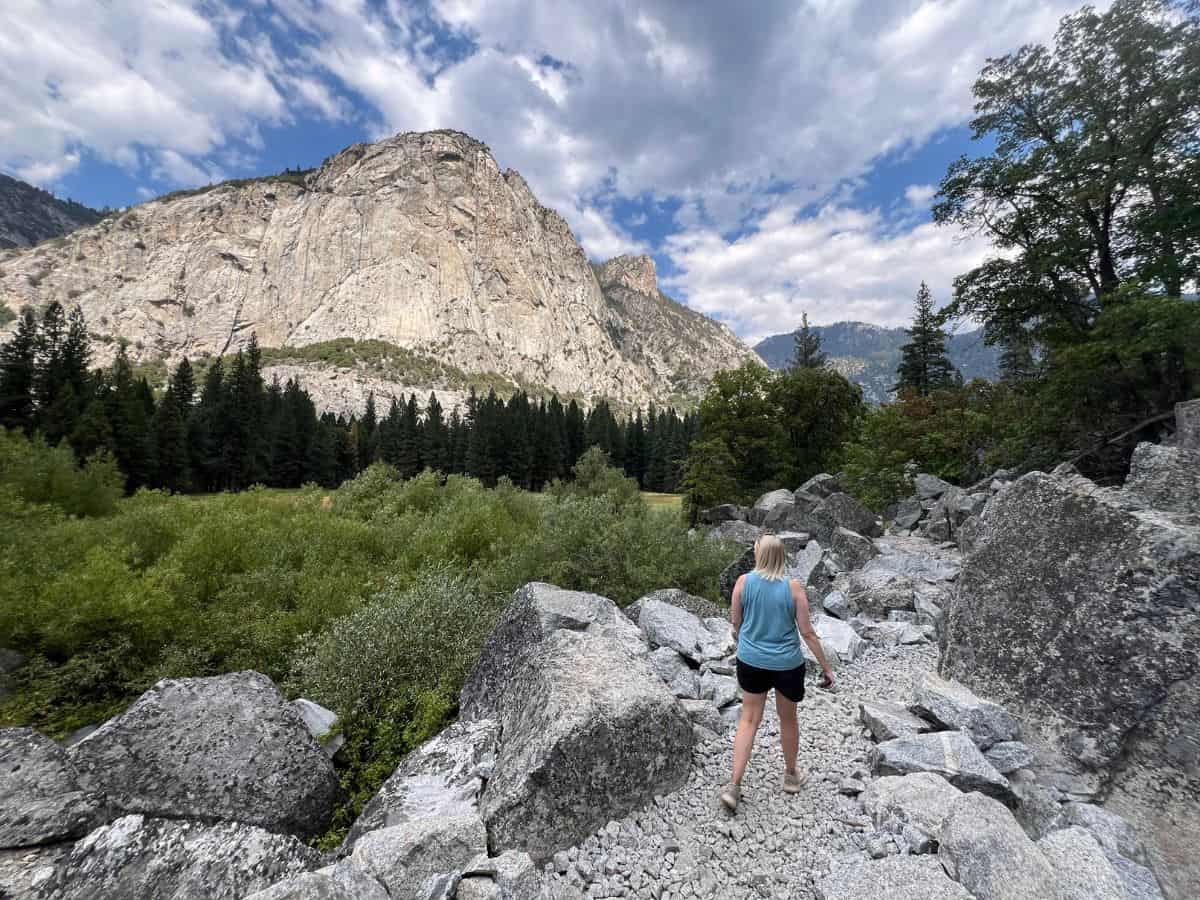 A woman hikes a trail through rugged granite rocks toward a mountain in the distance.