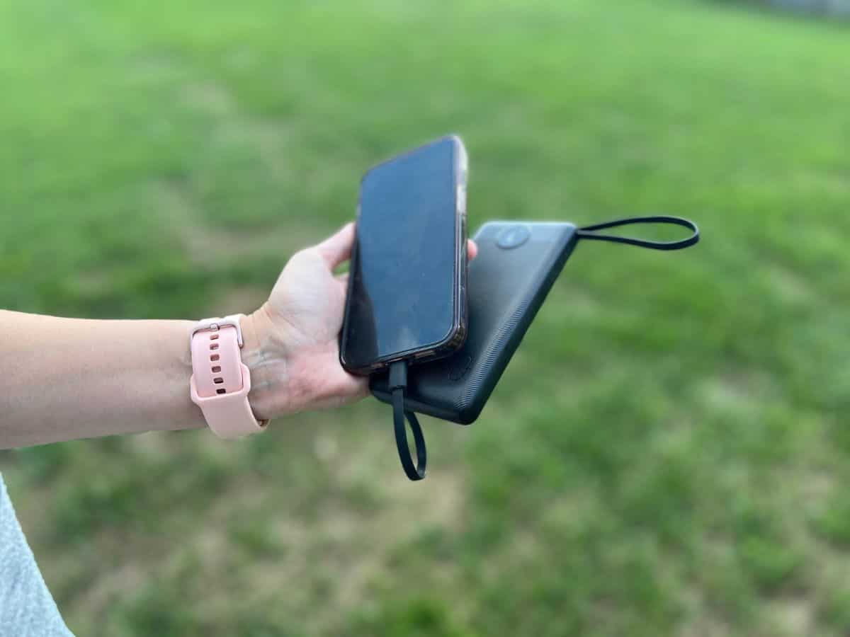 A woman's hand holds a cell phone and a portable charger.