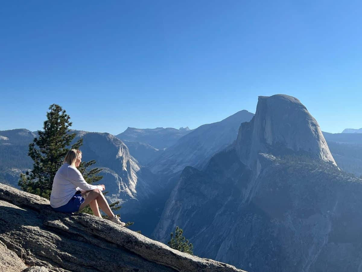 A woman sits at an overlook to enjoy views of towering granite cliffs.