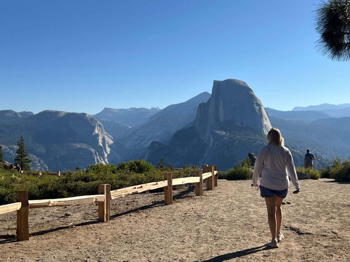 A woman walks toward an overlook where she can see large granite domes.