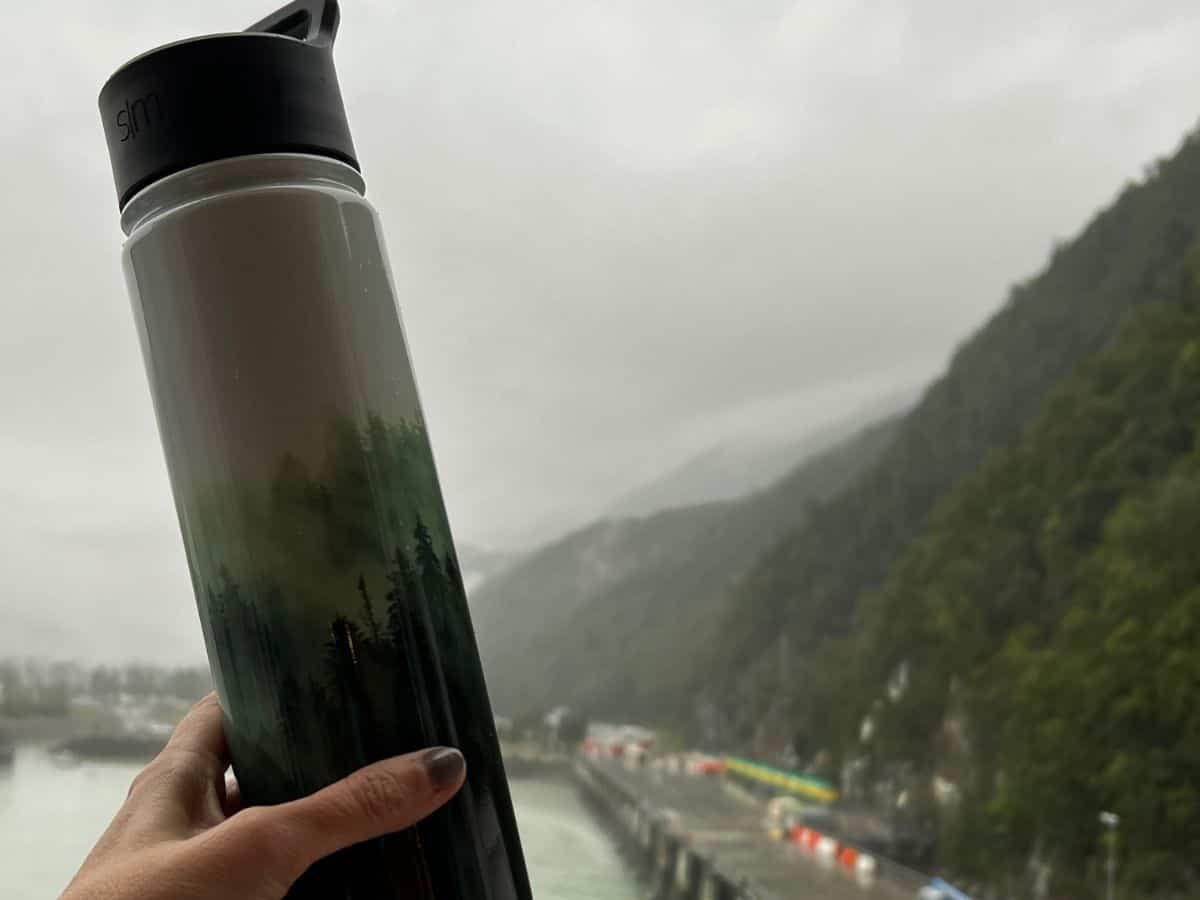 A woman's hand holds up a water bottle decorated with painted trees.