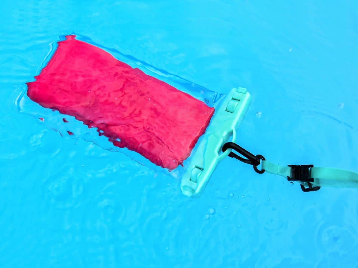 A pink phone in a waterproof phone pouch floats in a pool.