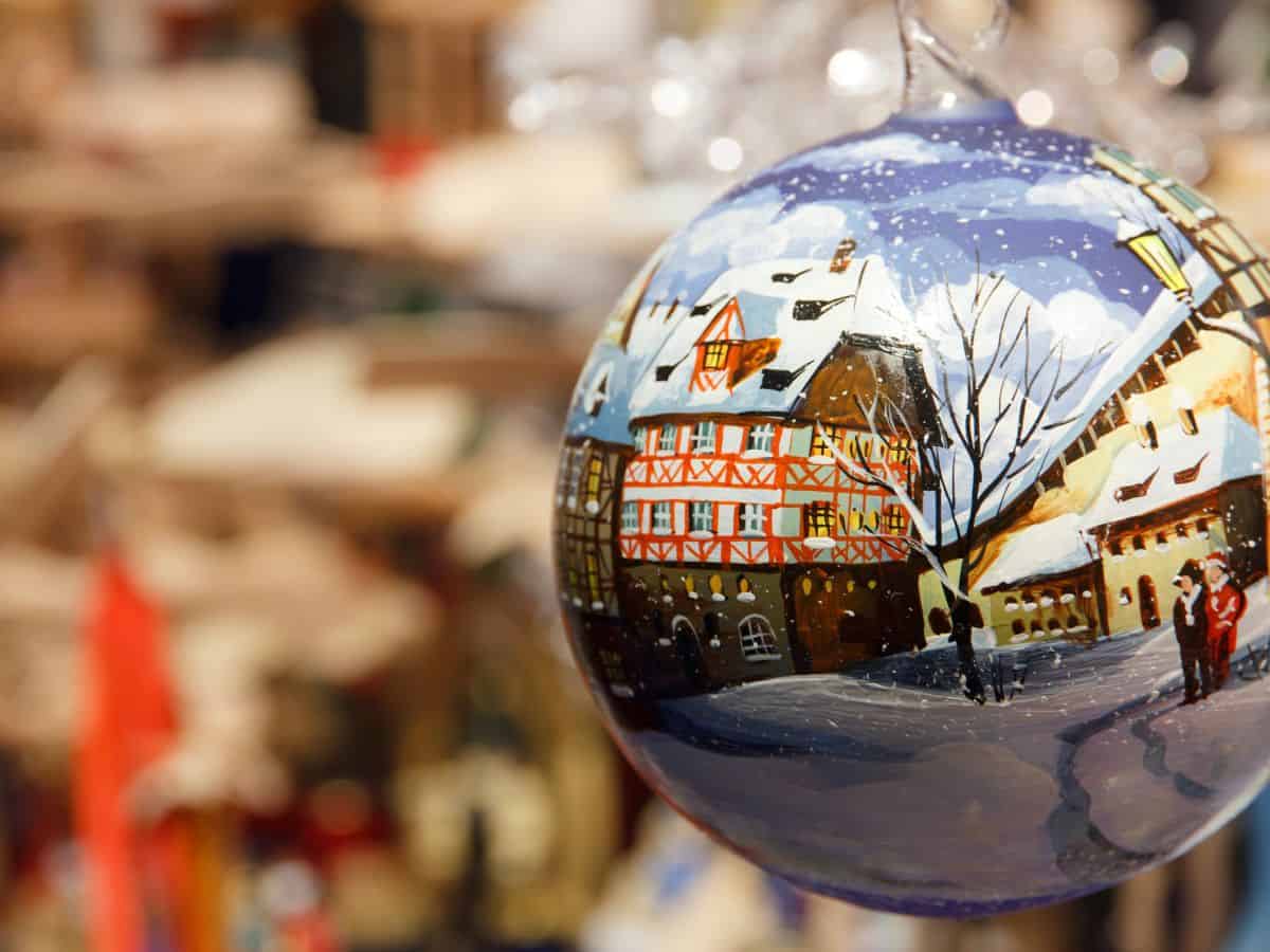 A round Christmas ornament depicts a Bavarian village