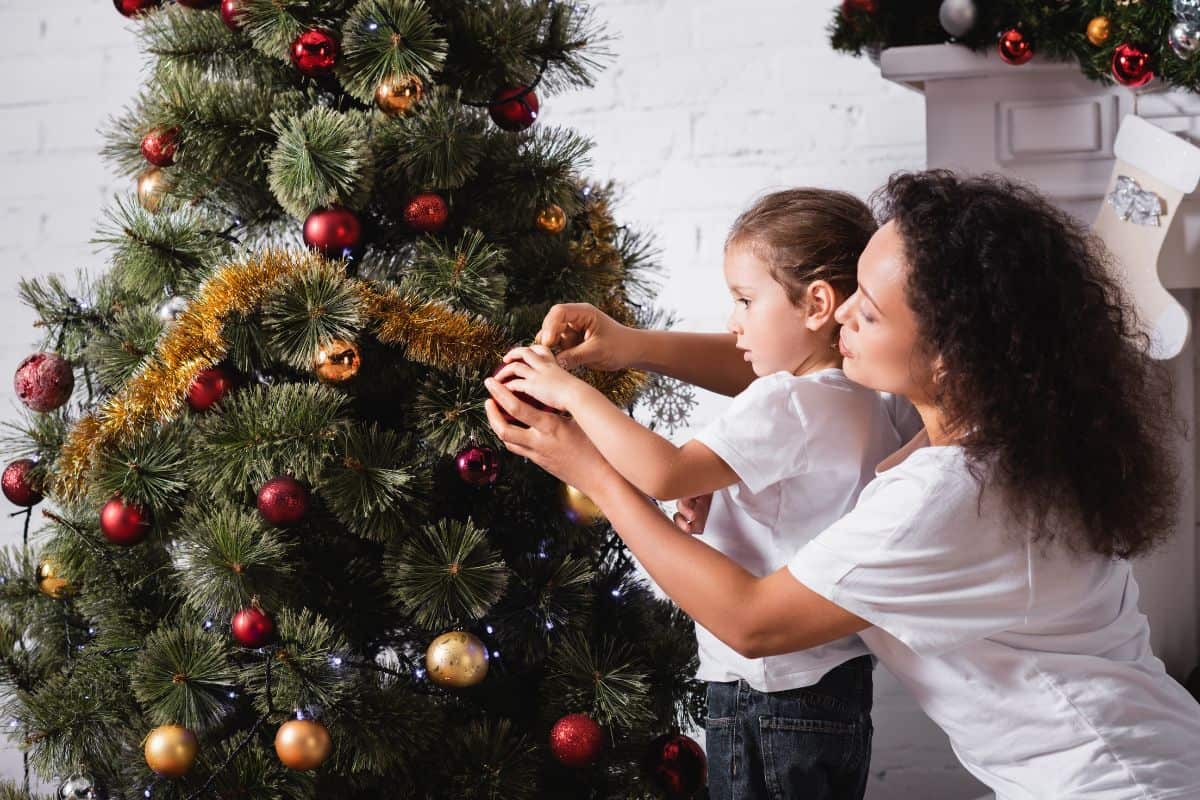 A mom helps her daughter put an ornament on a Christmas tree.