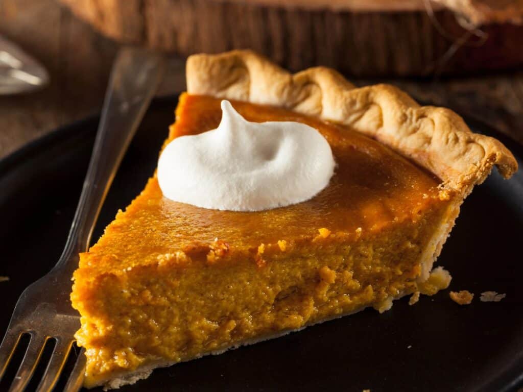 A slice of pumpkin pie topped with whipped cream sits on a small plate