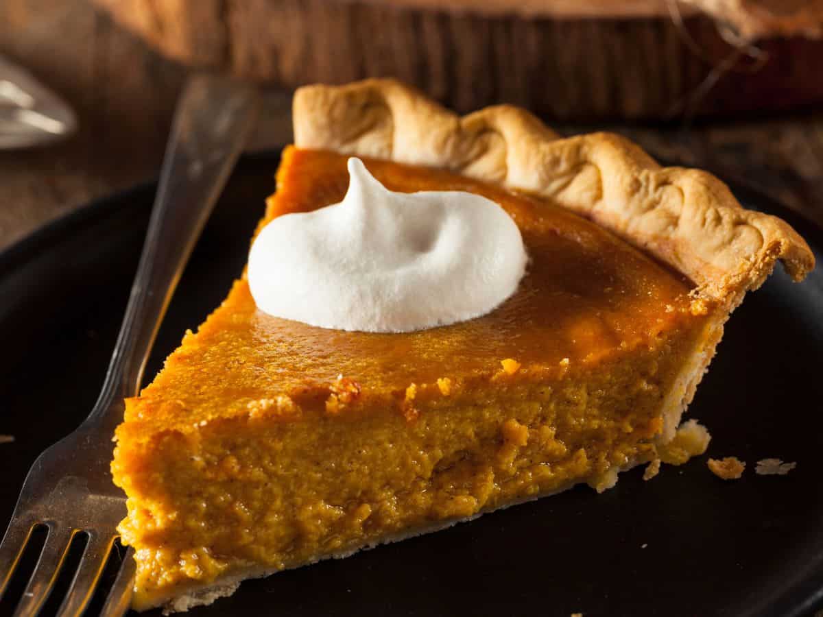 A slice of pumpkin pie topped with whipped cream sits on a small plate