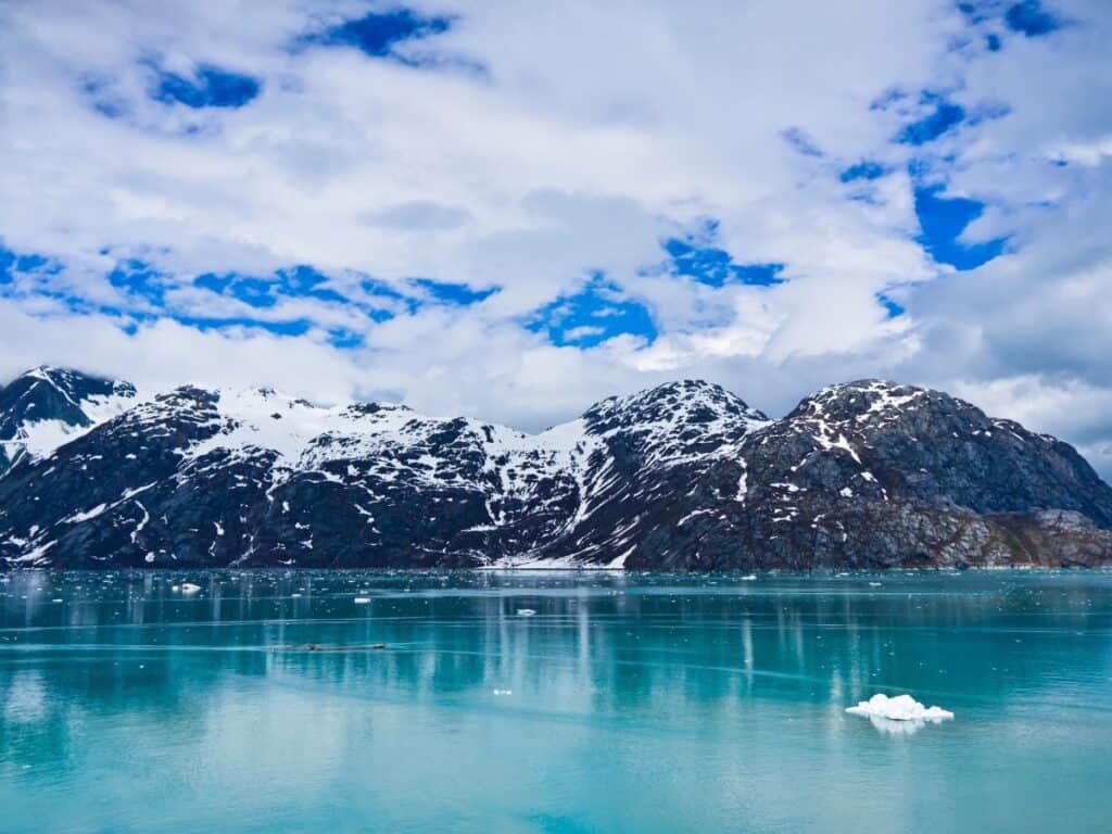 Icebergs float in turquoise water against a mountain backdrop