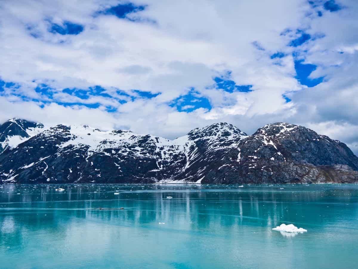 Icebergs float in turquoise water against a mountain backdrop