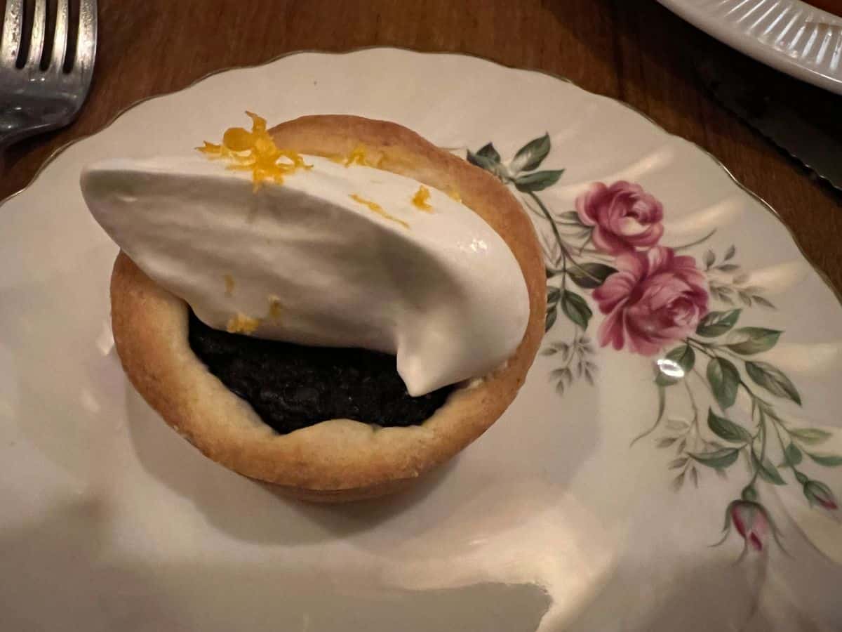 A Saskatoon berry tart topped with whipped cream sits on an antique plate
