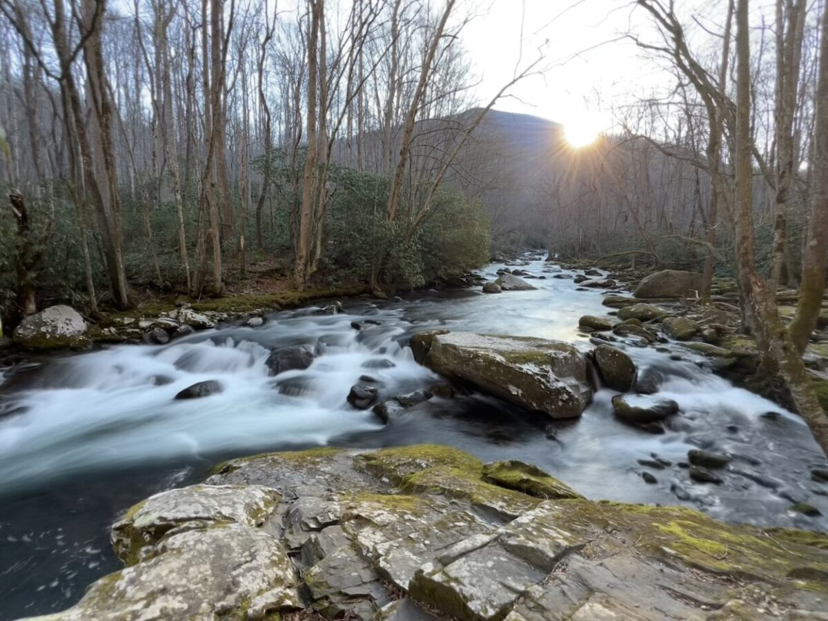 The sun rises over a mountain behind a rushing river