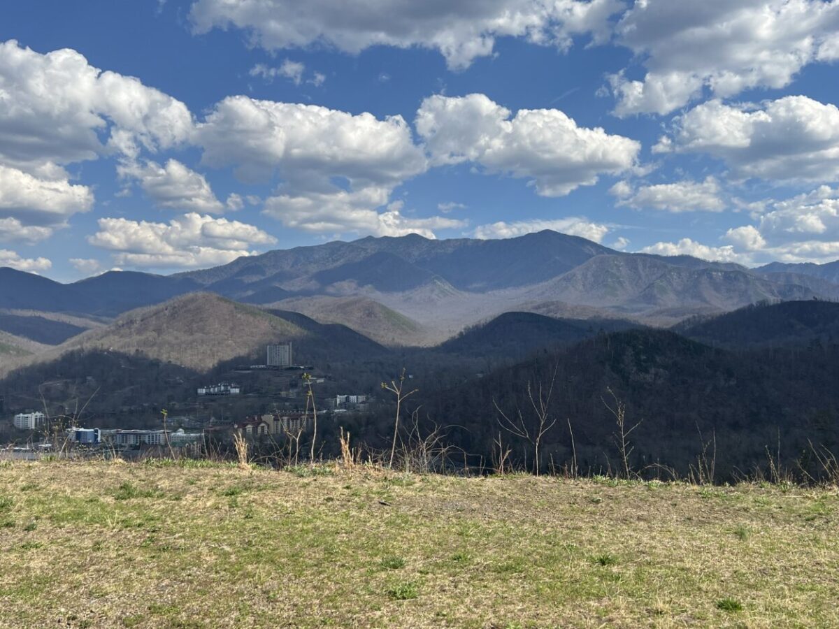 Big white puffy clouds cast shadows on a mountain range.