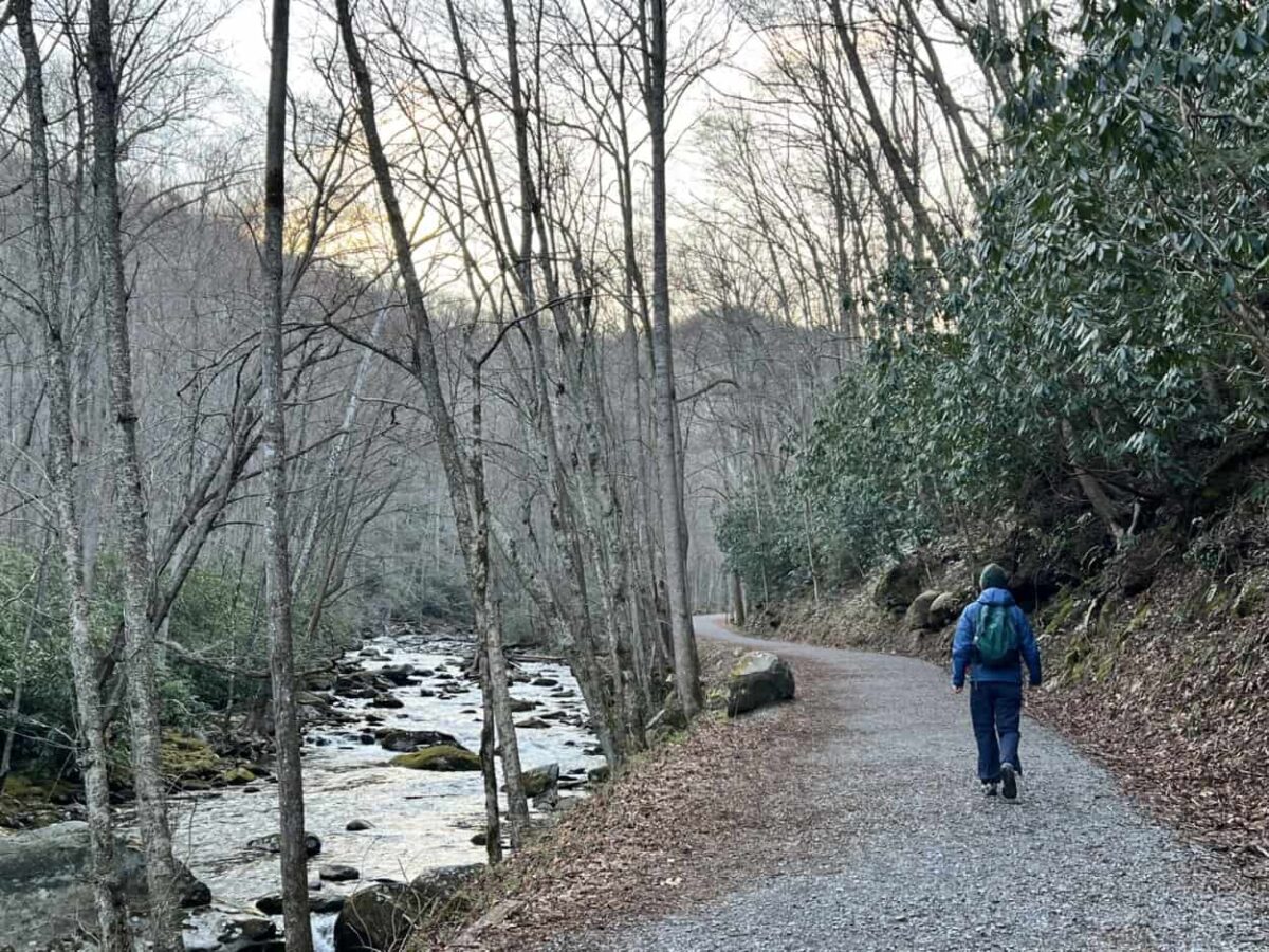 A man hikes a trail of crushed stone along a mountain river.