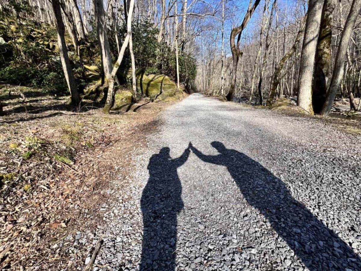 A shadow of a man and woman giving each other a high five shows on a hiking path in Great Smoky Mountains National Park