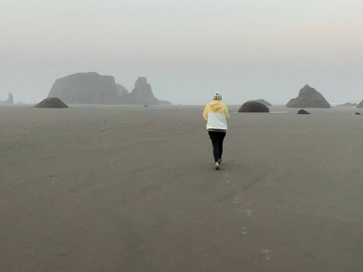 Why the Oregon Coast is special - sea stacks! A woman walks toward sea stacks on a foggy morning.