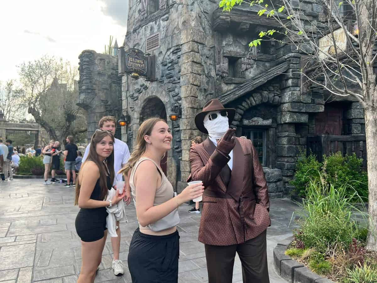The Invisible Man points up toward something while talking to a young girl in Epic Universe's Dark Universe.