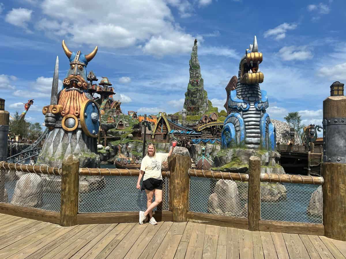 A woman raises a drink in front of two towering statues, one of a Viking, and the other of a dragon.