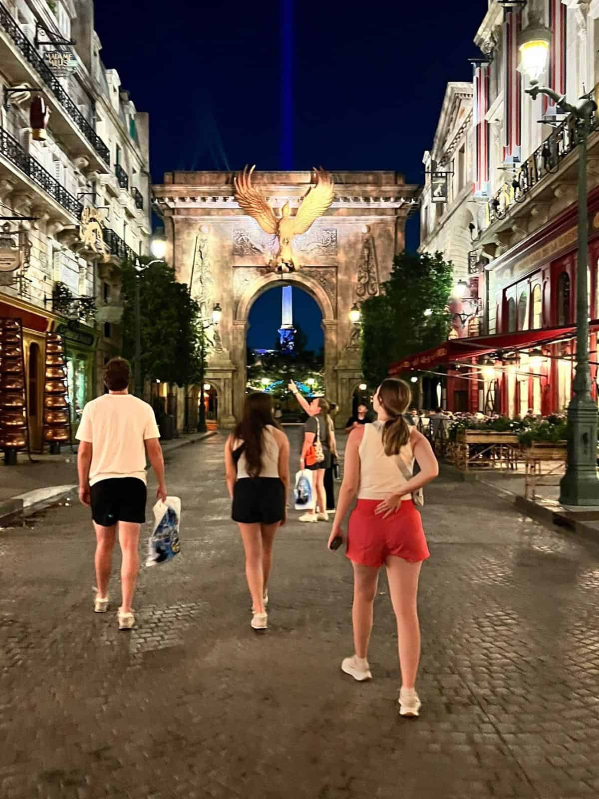 A man and two women walk toward a large arch that has a statue of a phoenix.